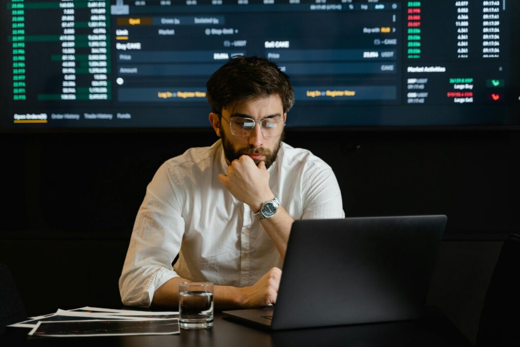 A man intensely analyzing stock market data on a laptop in an office setting.